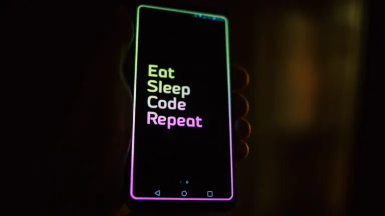 Smartfon trzymany w ciemności z napisem Eat Sleep Code Repeat na ekranie.