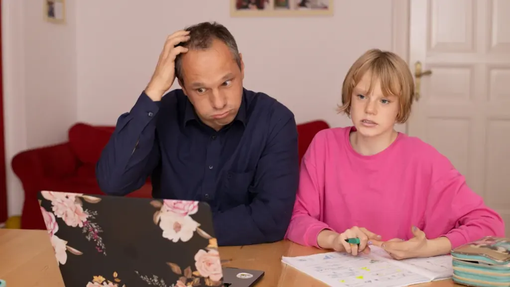 Zaniepokojony ojciec siedzący z córką przy laptopie podczas nauki w domu
