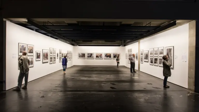 Widok na przestronną galerię sztuki z wiszącymi fotografiami i zwiedzającymi gośćmi w Toruniu.
