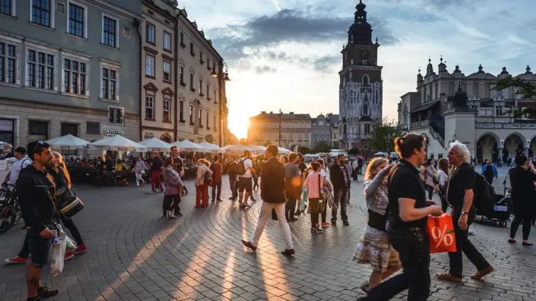 Turyści spacerujący po Rynku Głównym w Krakowie podczas słonecznego, gorącego dnia w Polsce.