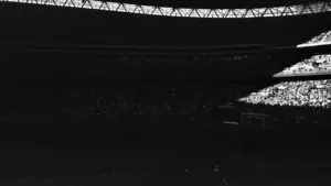 Ciemny, klimatyczny widok na wypełnione trybuny stadionu piłkarskiego w świetle reflektorów.
