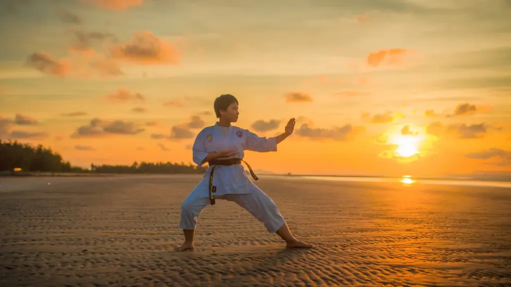Młody zawodnik wykonuje ćwiczenia taekwon-do na piaszczystej plaży podczas pięknego zachodu słońca.