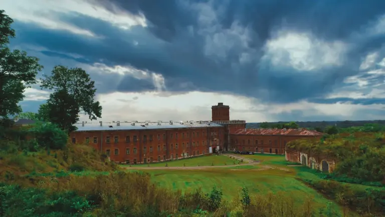 Historyczny budynek Twierdzy Modlin otoczony zielenią pod dramatycznym, zachmurzonym niebem w Polsce.