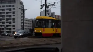 Charakterystyczny czerwono-żółty tramwaj warszawski przejeżdżający wieczorem na tle wieżowców w centrum Warszawy.