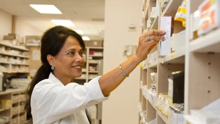 Farmaceutka sięgająca po leki z półki w profesjonalnej aptece podczas codziennej pracy.