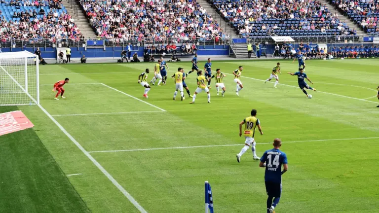 Piłkarze w trakcie emocjonującej akcji na zielonej murawie stadionu podczas profesjonalnego meczu piłkarskiego.