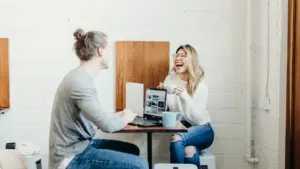 Para młodych ludzi rozmawiająca przy kawie i laptopie w jasnym wnętrzu kawiarni.