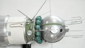 Model radzieckiego satelity z metalową sferą, antenami i zielonymi kulistymi zbiornikami na jasnym tle.